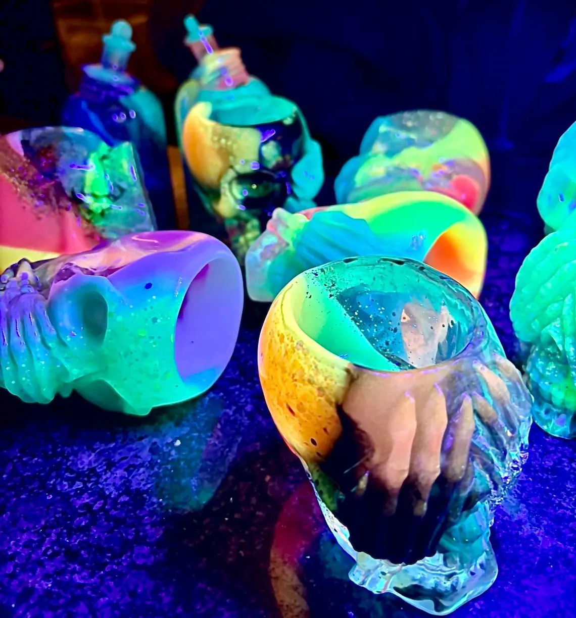 A crowd of neon resin skull cups glowing under blacklight