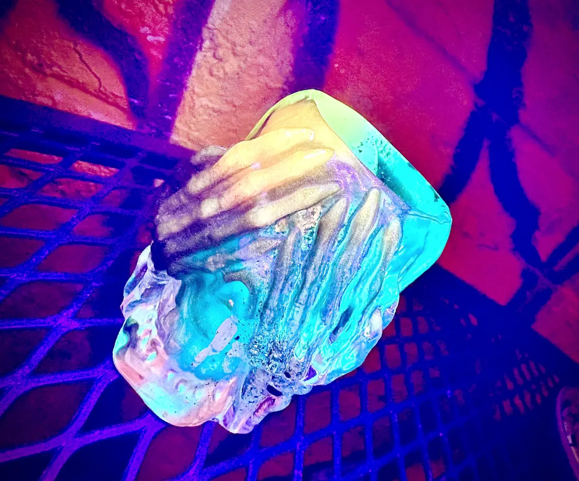 Turquoise and yellow resin skull cup resting on a purple-lit metal grate