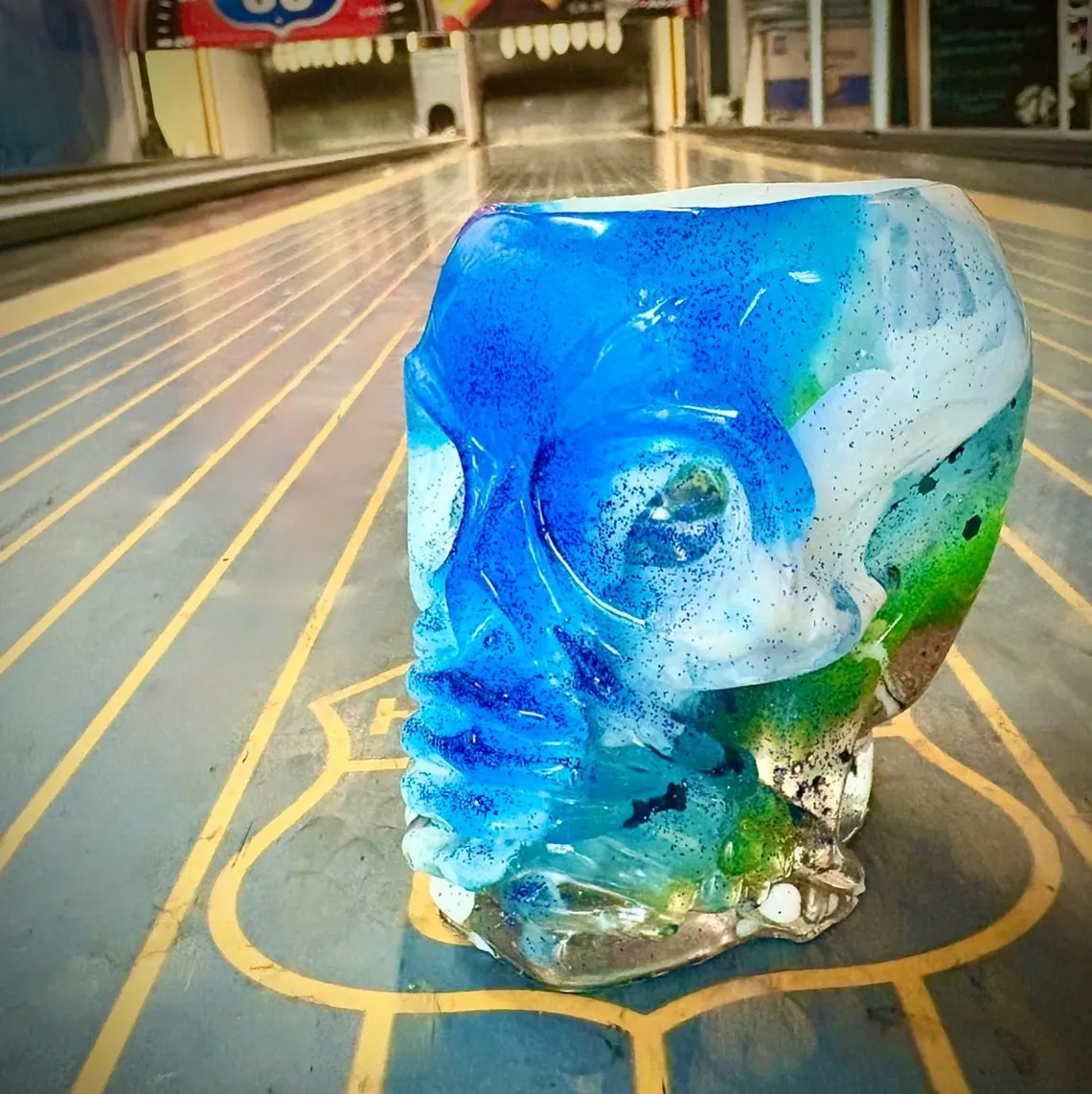 Blue and green glitter resin skull cup standing on a bowling lane