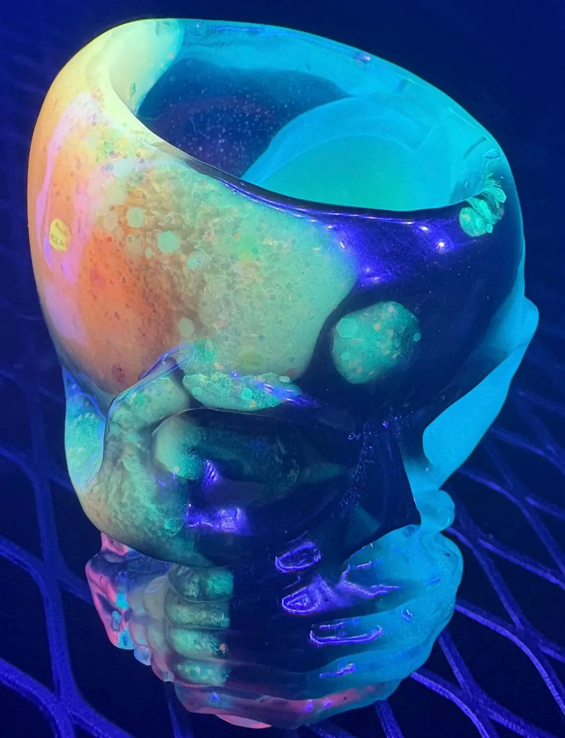 Glowing resin skull cup cradled by sculpted skeleton fingers under UV light